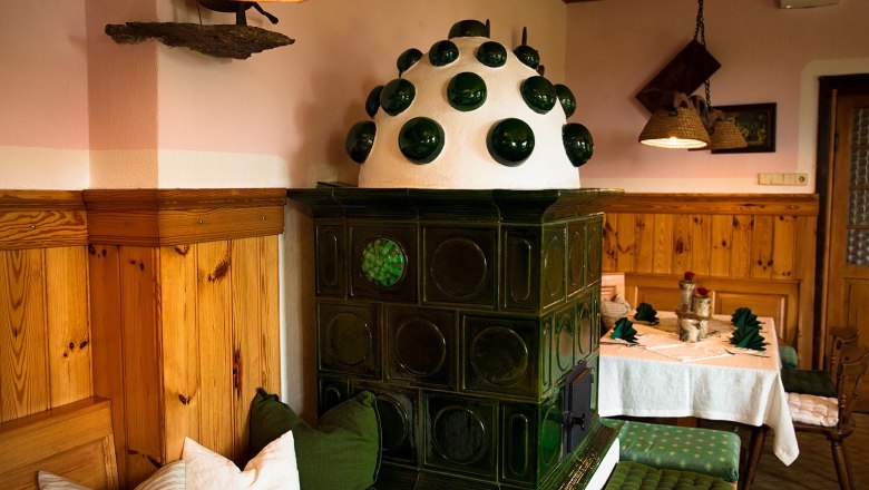 Restaurant, © Kloster NaturSinne Cozy, traditional parlor with green tiled stove and wooden furniture.
