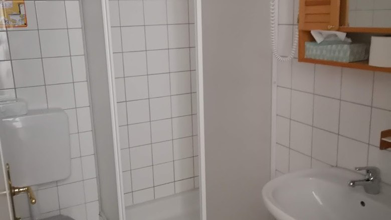 Fürdőszoba, © Karl Buchner Egy kis, fehér csempézett fürdőszoba zuhanyzóval, WC-vel és mosdókagylóval.