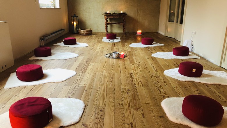 Sacred space, © Kloster NaturSinne Meditation room with red cushions on white mats, candles and wooden floor.