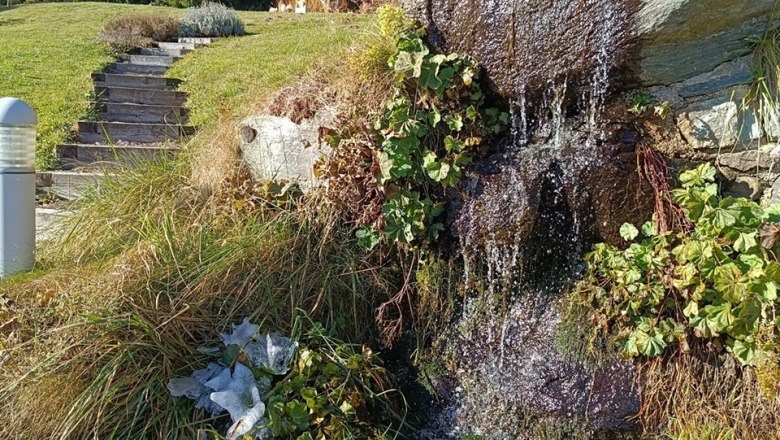 Herbst in Mönichkirchen, © Glamping-Park Mönichkirchen OG Kleiner Wasserfall in herbstlicher Landschaft mit Bäumen und blauem Himmel.