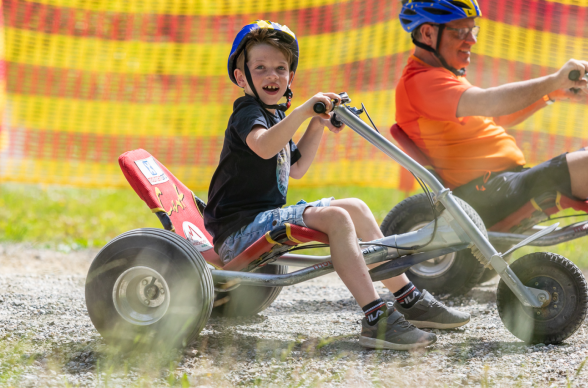 Kind sitzt auf Mountaincart und steht, © Christian Kremsl Mountaincartfahren für Kinder