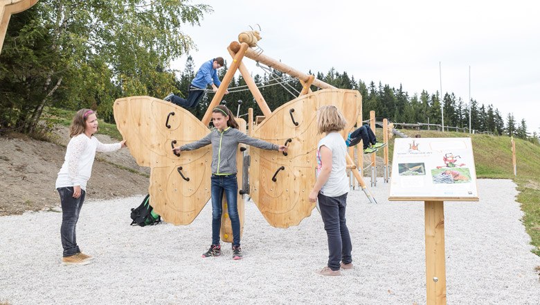 There is a lot to discover along the ant trail, © Gerhard Buchacher Children play on a large wooden butterfly in an outdoor playground.