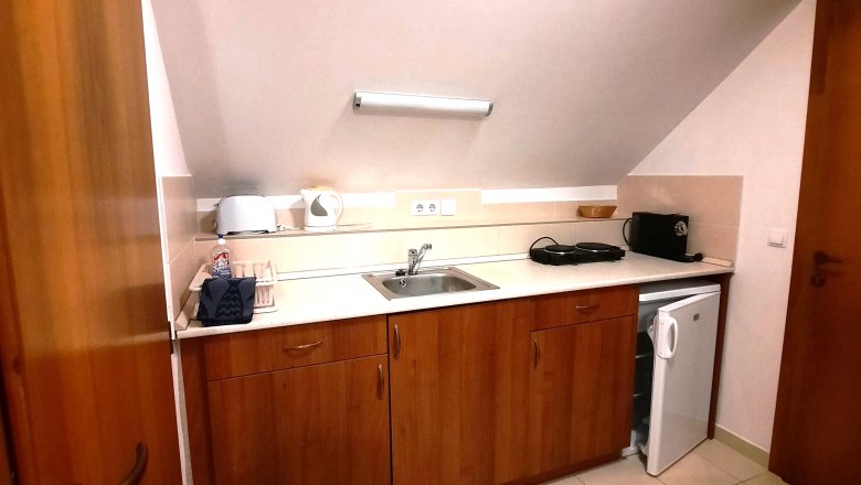 Küchenzeile, © Ildiko Davidne Nagy Kleine Küchenzeile mit Holzschränken, Spüle, Toaster, Wasserkocher und Mini-Kühlschrank unter einer Dachschräge.