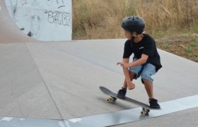 Ein Kind mit Helm f&auml;hrt auf einem Skateboard in einem Skatepark.