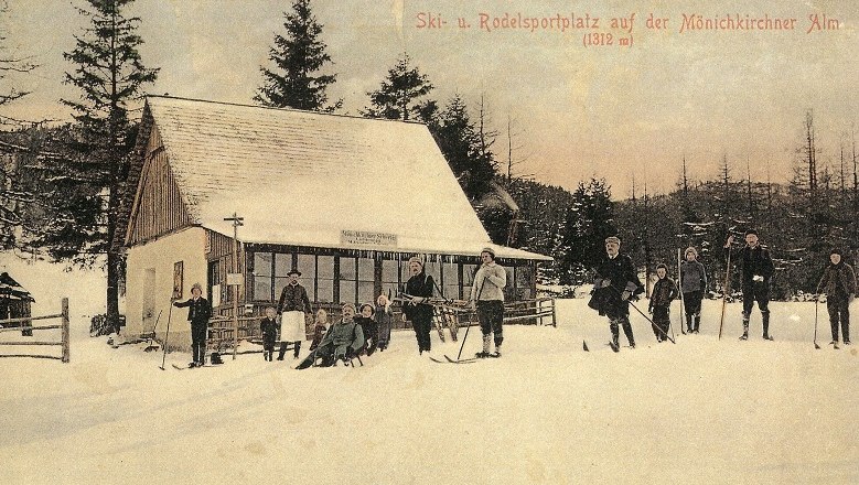 Historische Postkarte eines Skigebiets mit Menschen auf Skiern vor einer H&uuml;tte im Schnee.