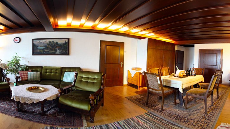 Cozy living room with wooden furniture, green sofa, dining table and carpets.