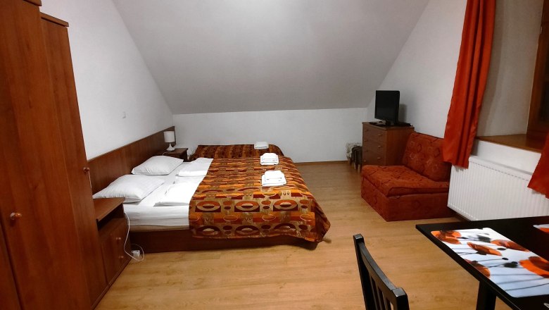 A simply furnished room with a double bed, sofa, table and chair. Wooden furniture and orange curtains dominate the room.