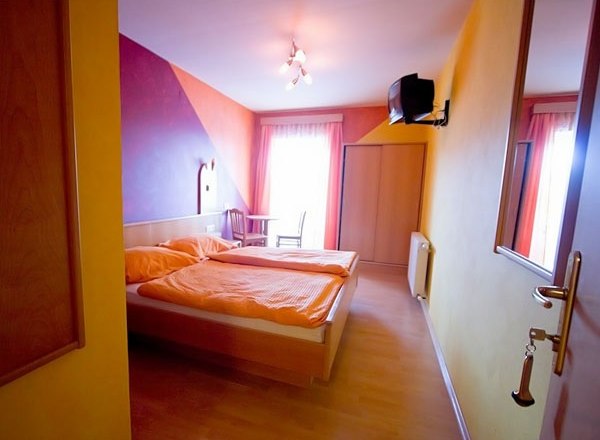 A cozy guest room with a double bed, colorful walls and a small TV on the wall.