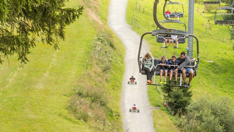 Familie auf Sessellift über grüne Landschaft.