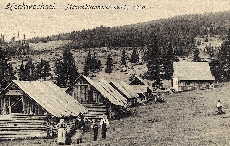 Historische Aufnahme von Holzhütten auf der Mönichkirchner Schwaig, umgeben von Wald und Wiesen, mit Menschen im Vordergrund.
