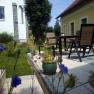 Terrace with table, chairs and plants in a garden next to a yellow house.
