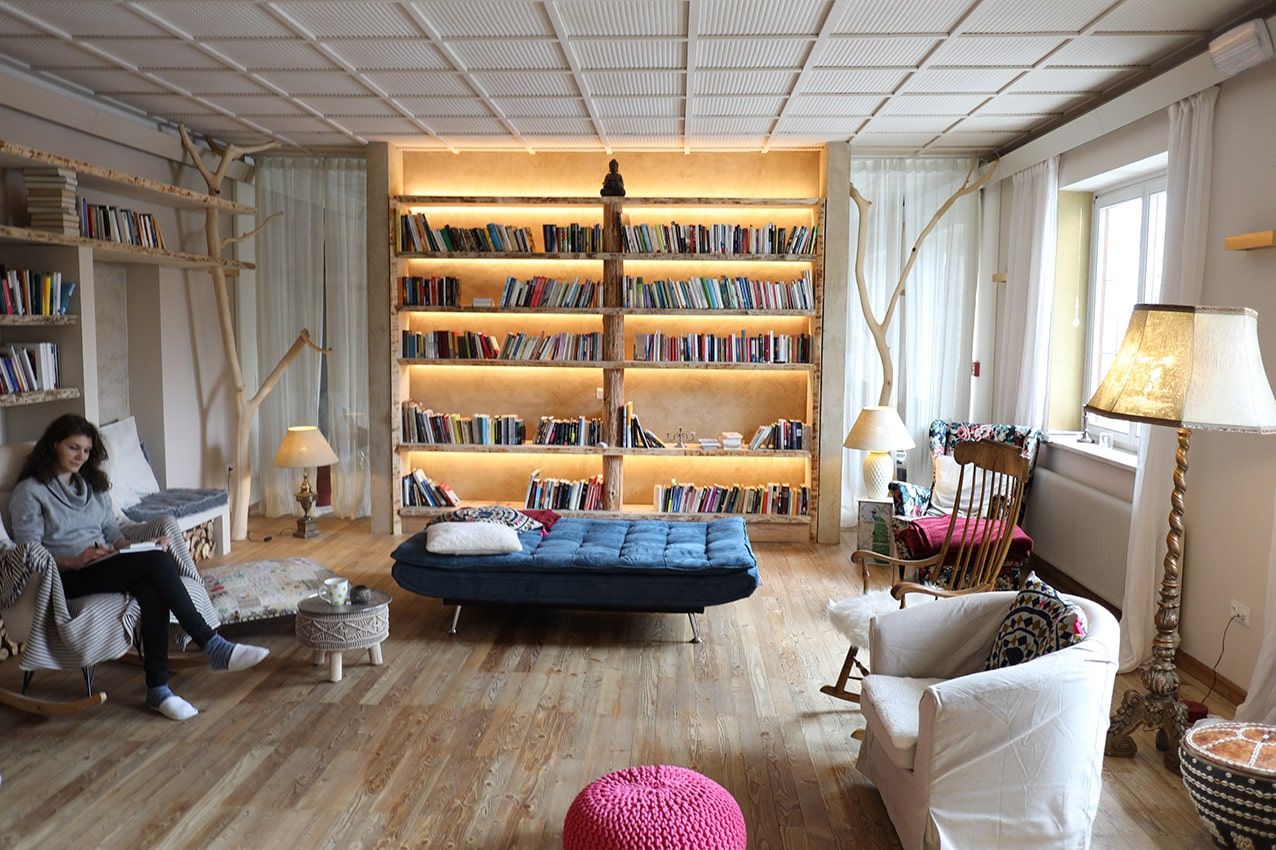 Gemütliche Bibliothek mit großen, beleuchteten Bücherregal, Sesseln und einer Person, die liest.
