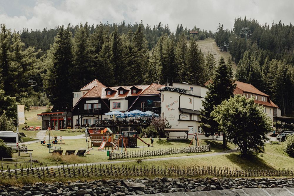 Ein Gasthaus in einer bergigen Landschaft mit Spielplatz und Wald im Hintergrund.