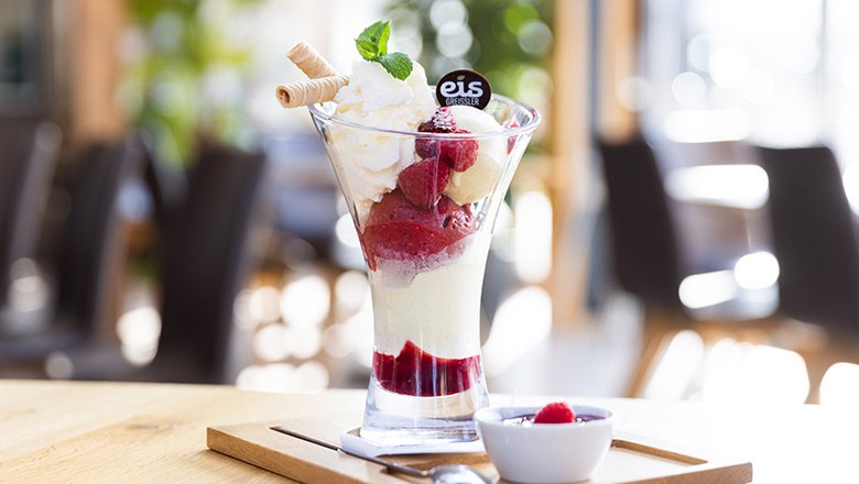 A sundae with fruit ice cream, whipped cream, waffles and raspberries on a wooden board., &copy; Blochberger Eisproduktion GmbH