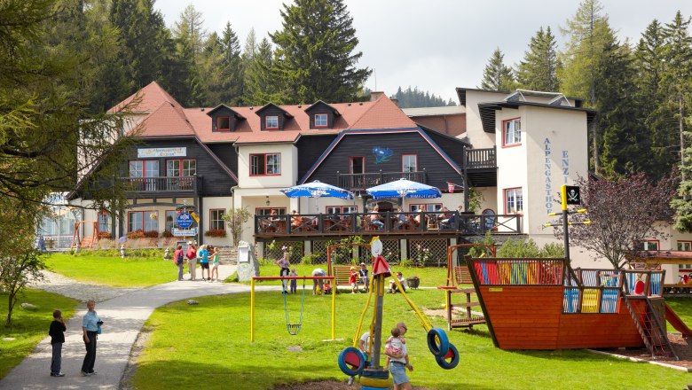 Alpengasthof Enzian, © Alpengasthof Enzian Ein Gasthof in den Alpen mit Spielplatz und Menschen im Freien.