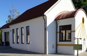 Wei&szlig;e Kapelle mit rotem Dach und gelben Akzenten, umgeben von gepflastertem Boden und Pflanzen.