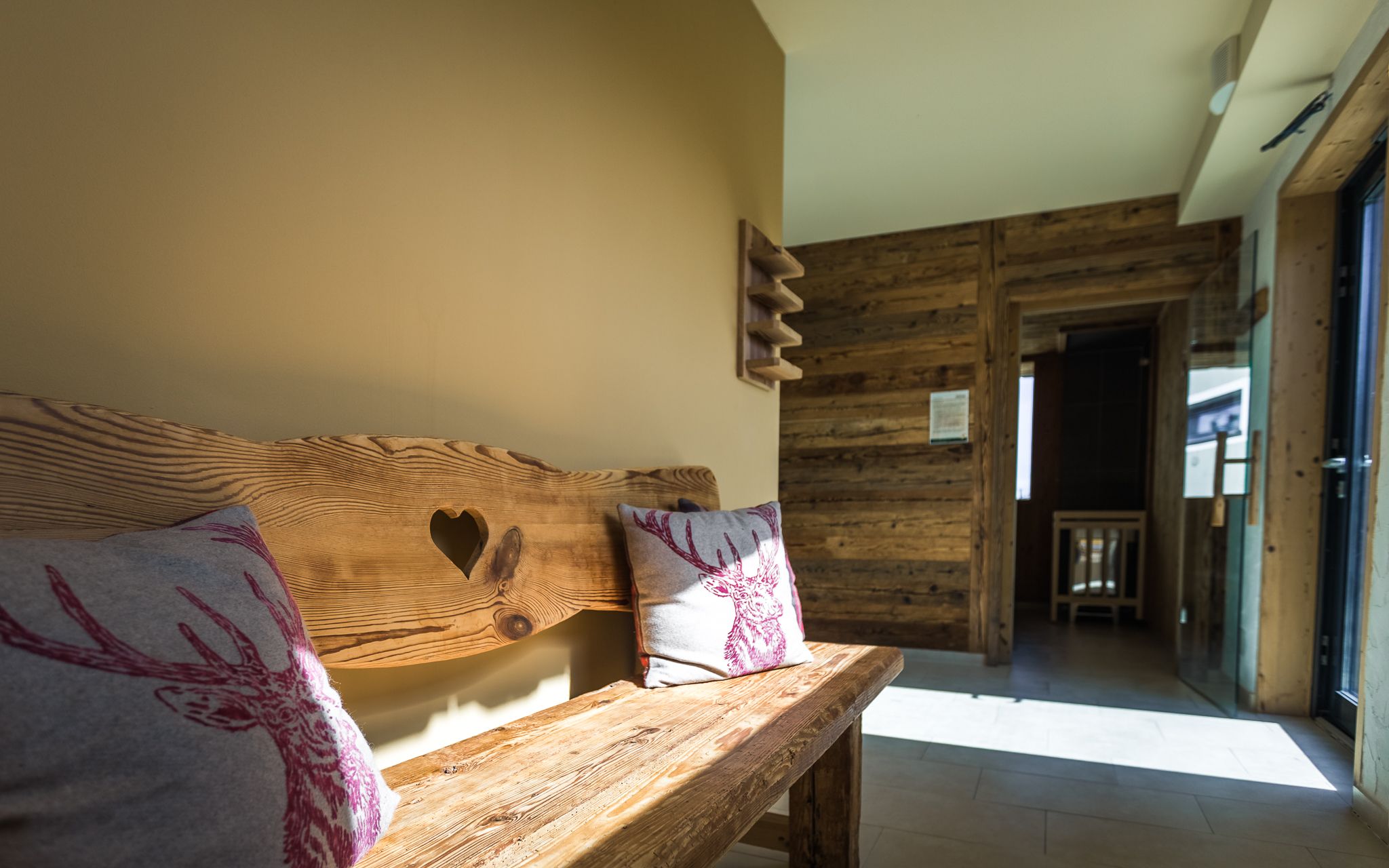 Rustikale Holzbank mit Herzmotiv und Hirschkissen in einem sonnigen Raum mit Holzwänden.