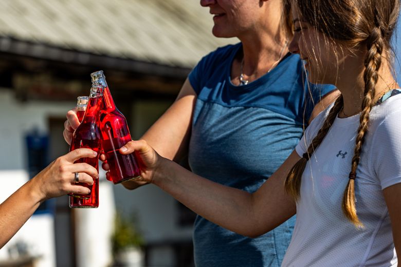 Drei Personen stoßen mit roten Getränkeflaschen an.