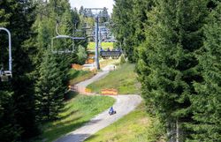 Ein Sessellift fährt über eine kurvige Mountaincartstrecke, die sich durch die Landschaft schlängelt. Die Strecke verläuft unterhalb der Liftanlage.