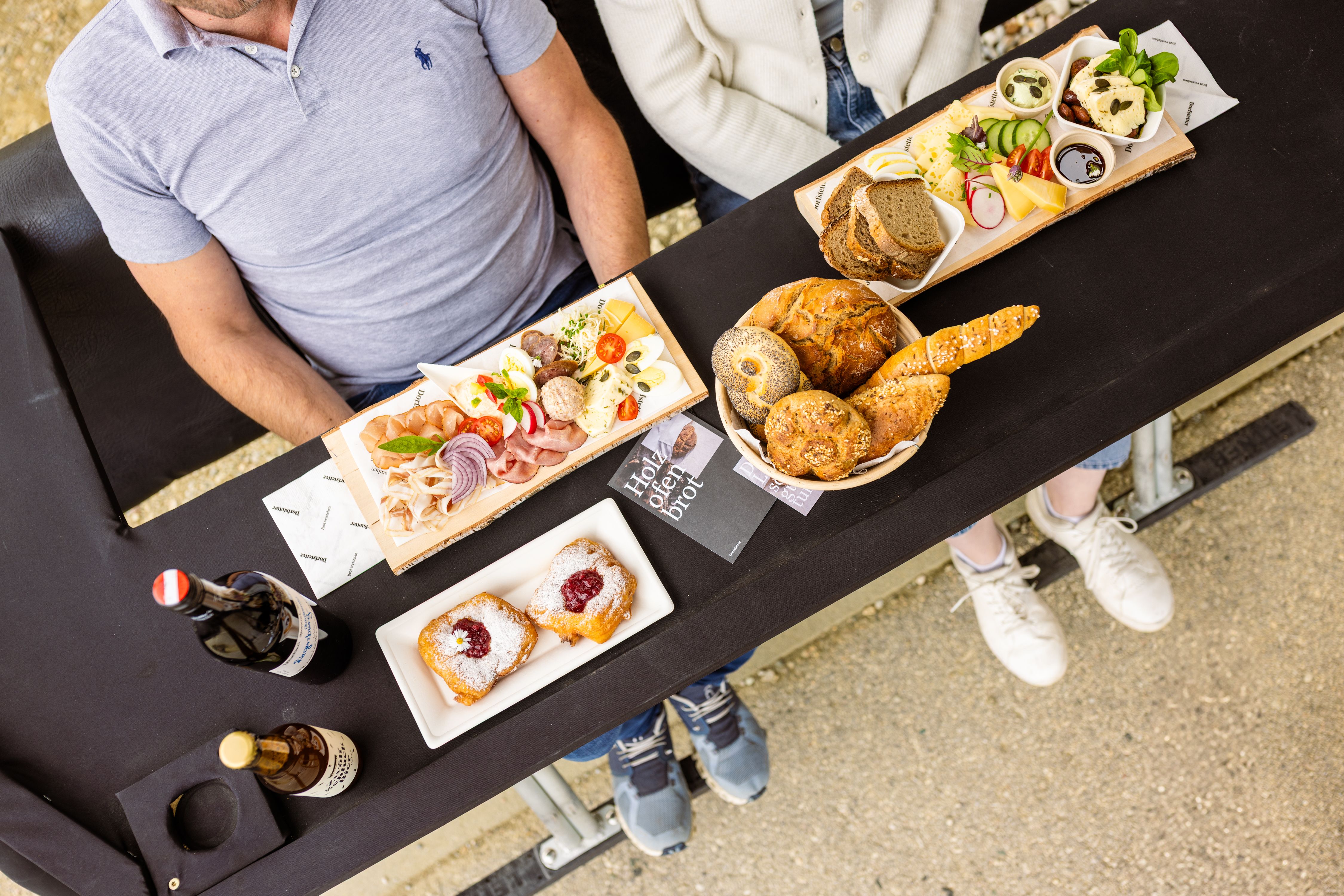 Von oben sieht man eine liebevoll und appetitlich arrangierte Jause auf dem Tisch eines Sessellifts. Verschiedene regionale Speisen und Getränke sind dekorativ angerichtet.