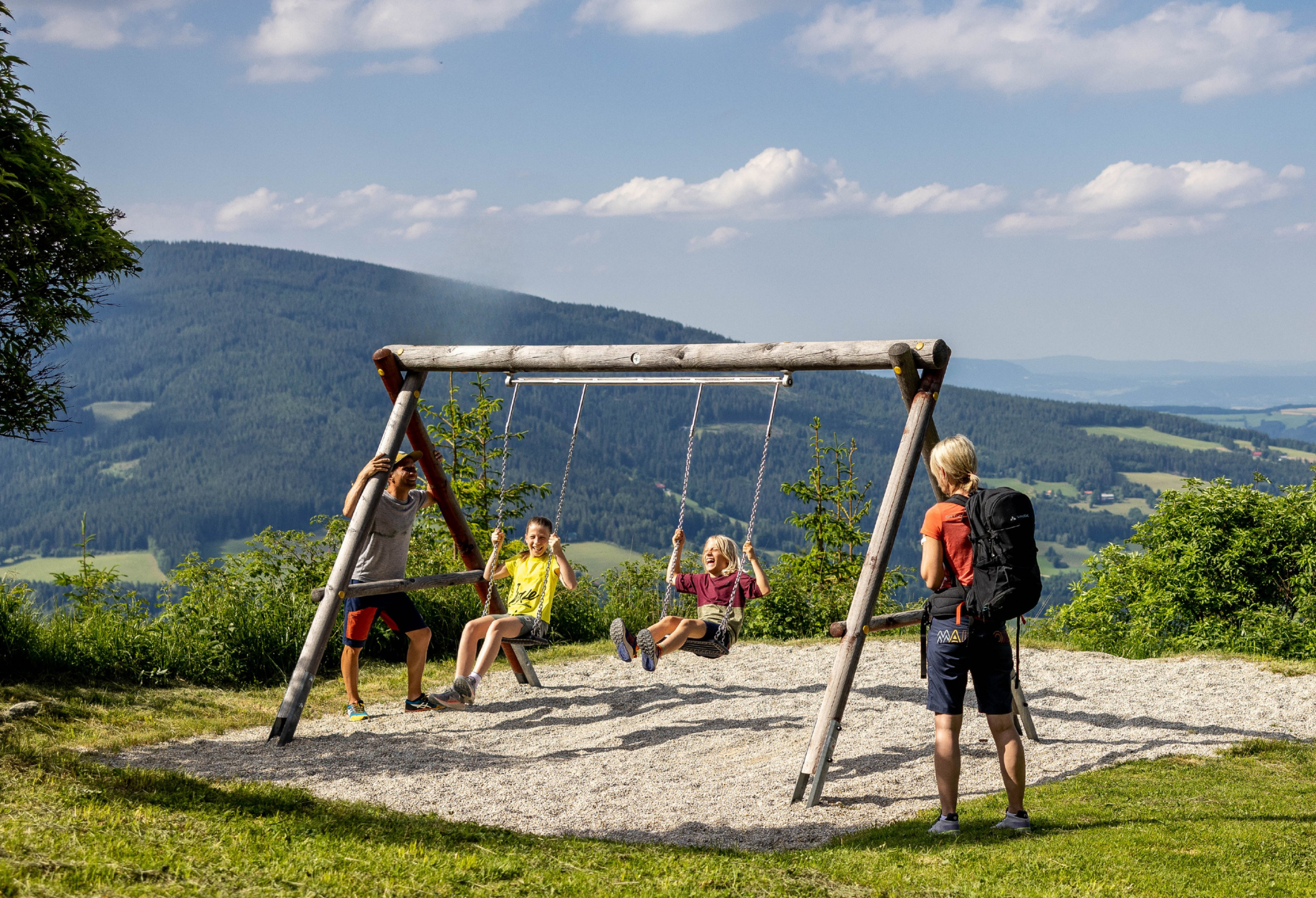 Zwei Kinder schaukeln und Eltern sehen zu