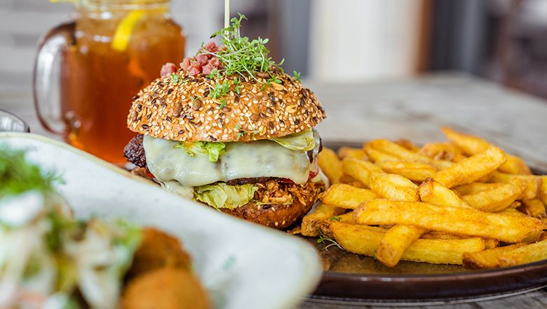 Ein Teller mit Burger und Pommes, im Hintergrund ein Getränk mit Zitrone.