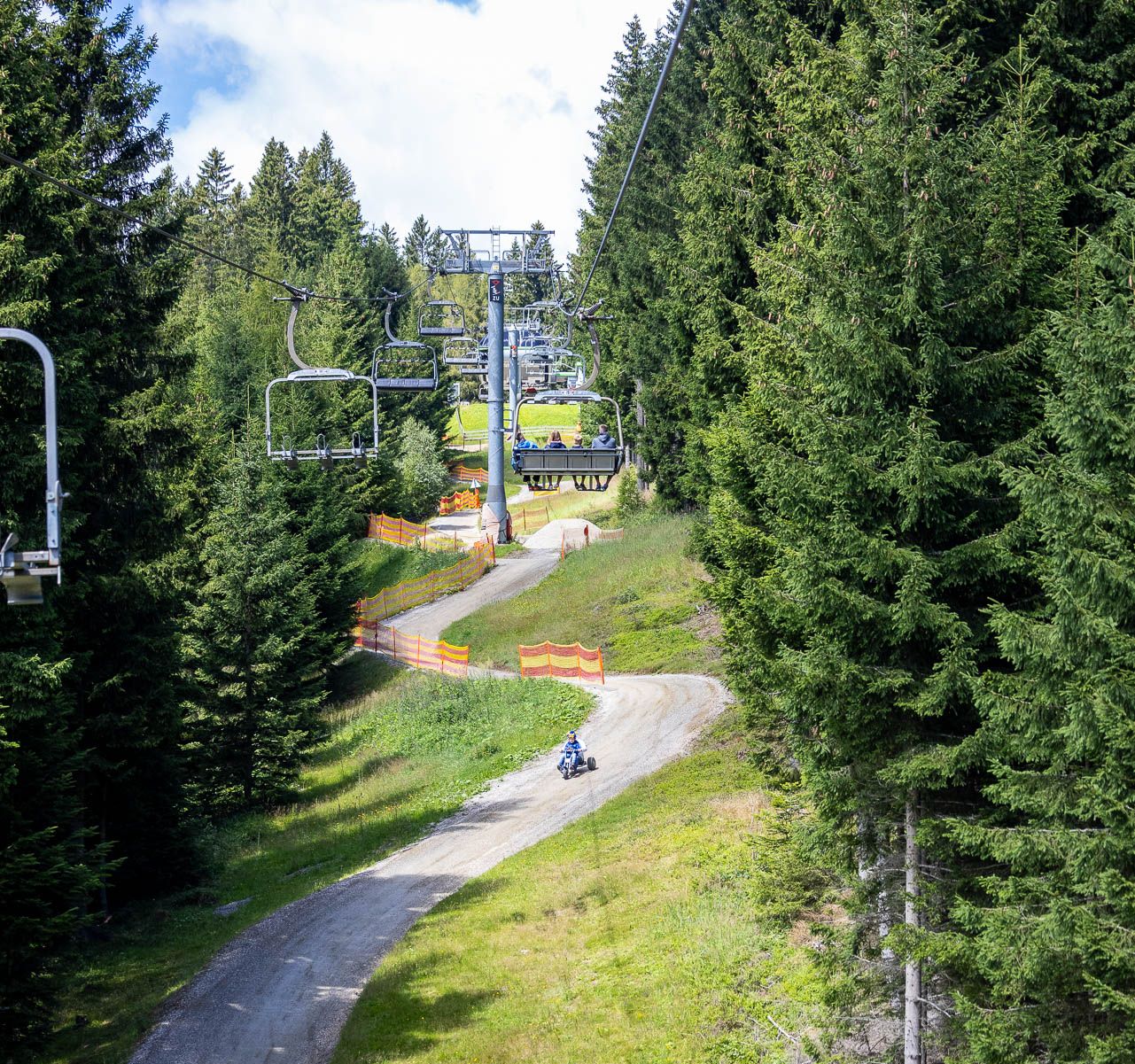 Ein Sessellift fährt über eine kurvige Mountaincartstrecke, die sich durch die Landschaft schlängelt. Die Strecke verläuft unterhalb der Liftanlage.