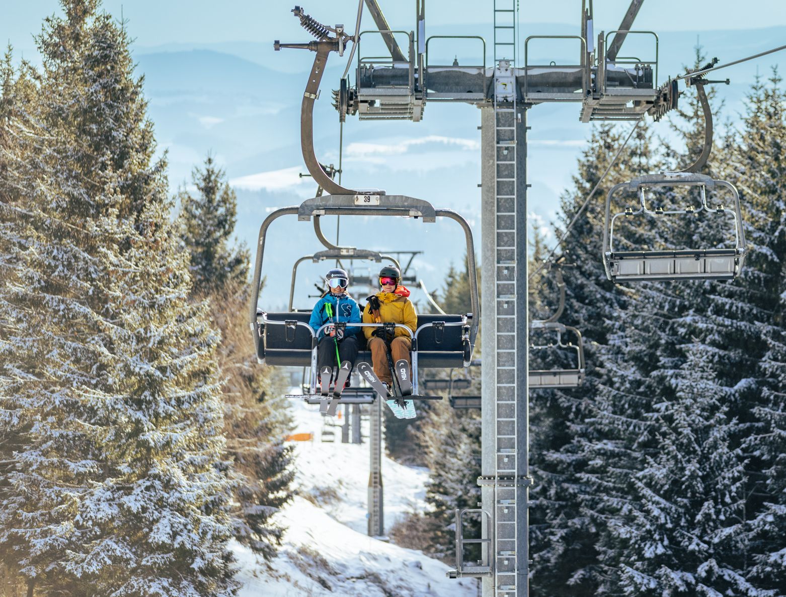 Zwei Damen fahren gemeinsam mit dem Sessellift auf den Berg um Skizufahren.