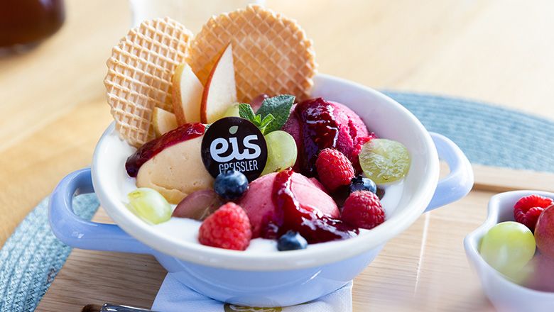 Eisbecher mit Joghurt, Fruchteis, Früchten und Waffeln auf einem Holzbrett.