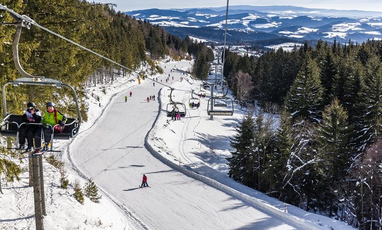 Skigebiet mit Sessellift und Skifahrern, umgeben von schneebedeckten Bäumen und Hügeln.