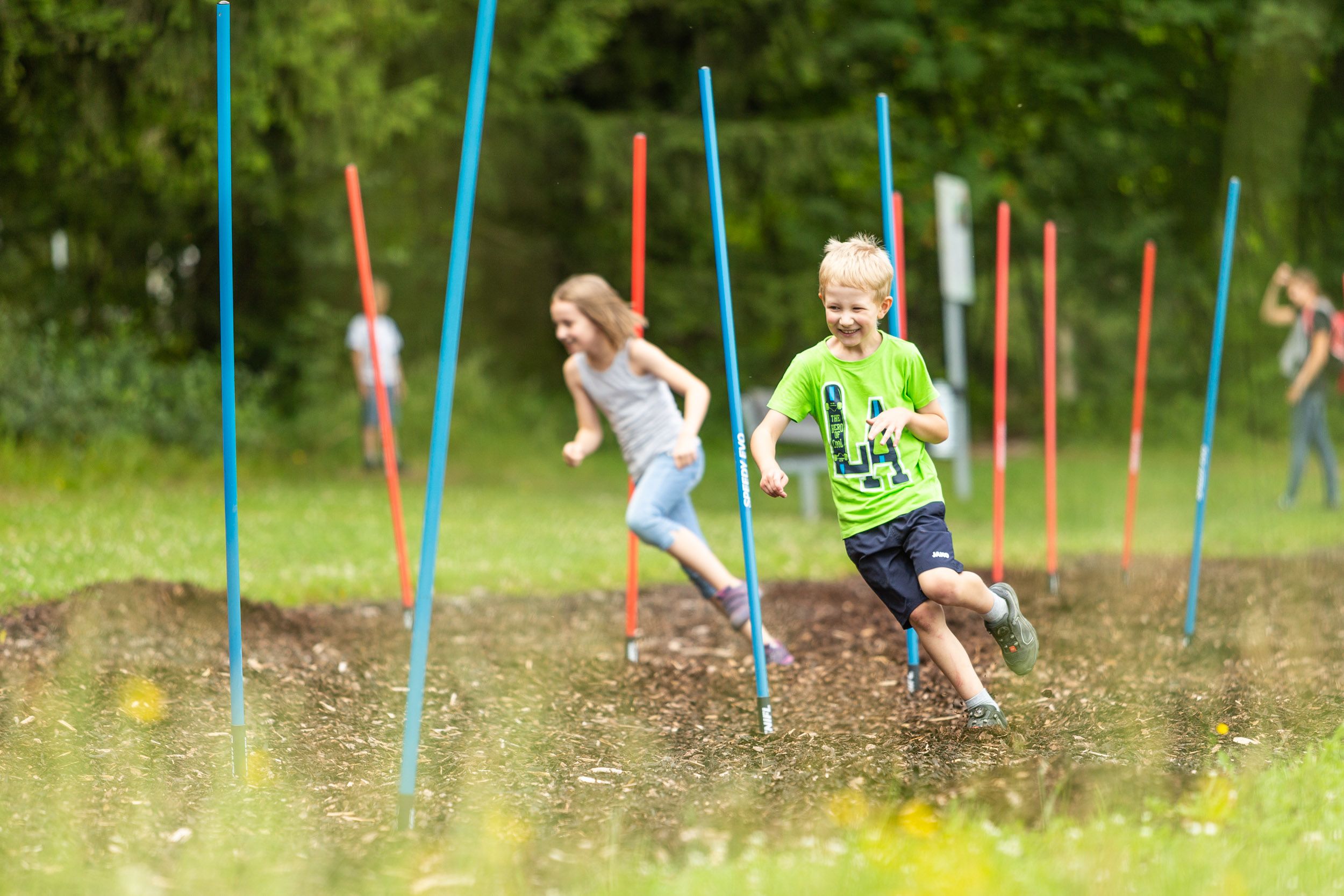 Kinder laufen durch einen Parcours mit bunten Stangen im Motorikpark St. Corona.