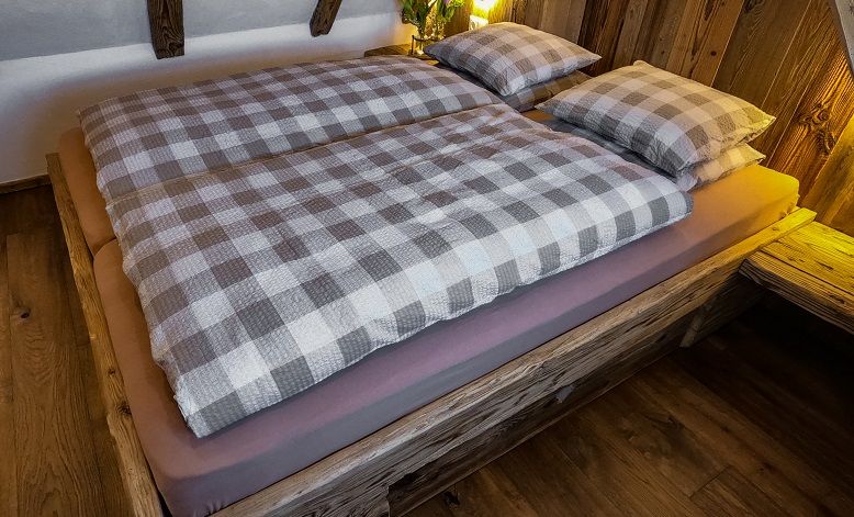 Gemütliches Bett mit kariertem Bettzeug in einer Holzhütte.