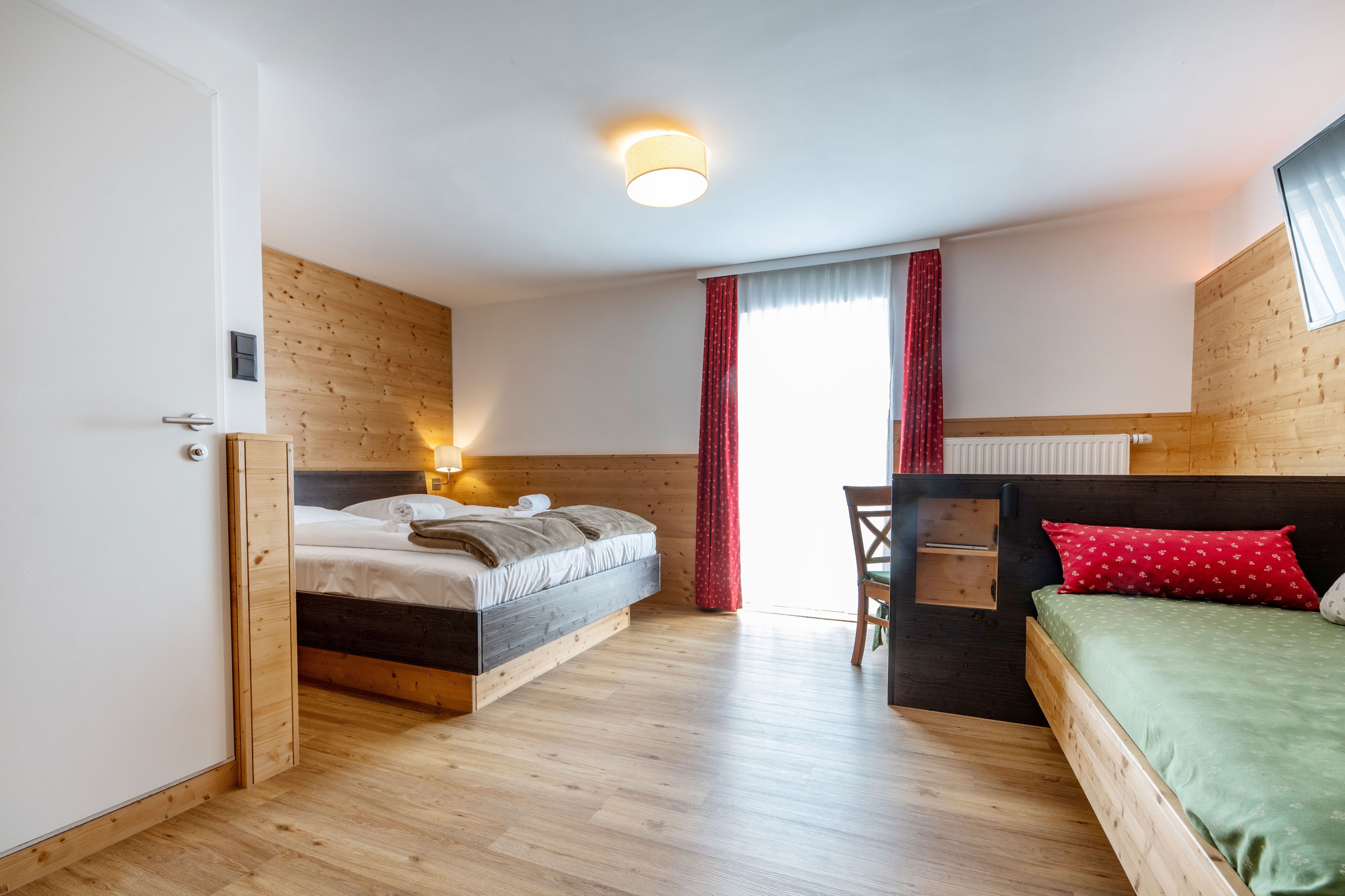 Gemütliches Hotelzimmer mit Holzwänden, Doppelbett, Einzelbett und rotem Vorhang.