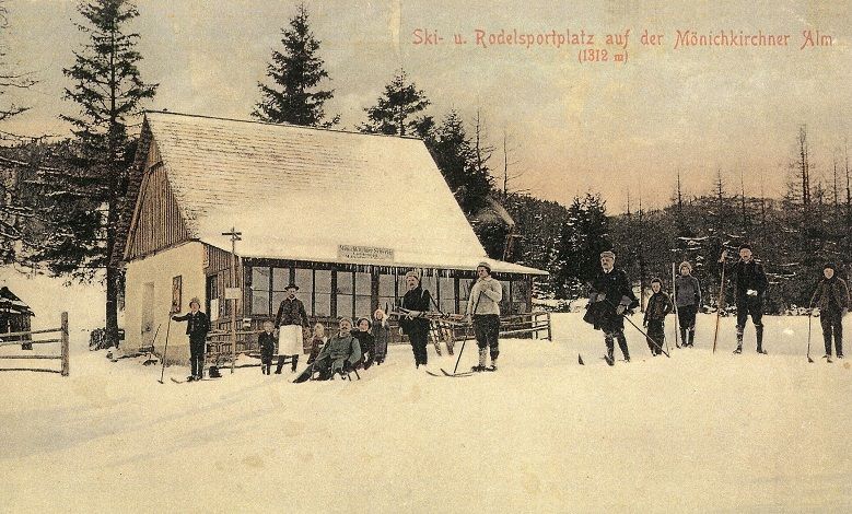 Historische Postkarte eines Skigebiets mit Menschen auf Skiern vor einer Hütte im Schnee.