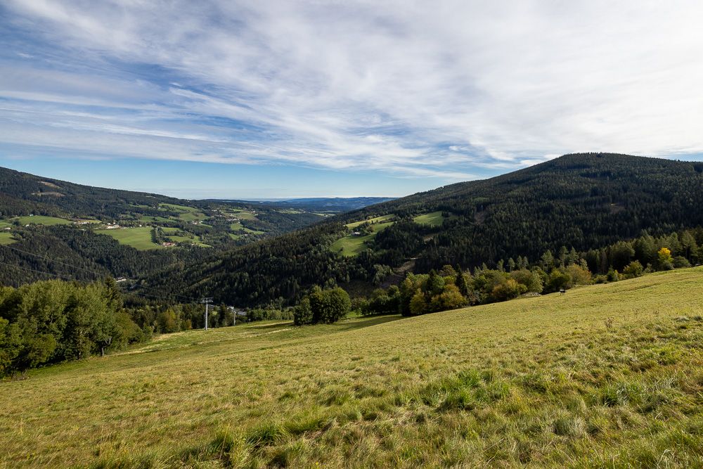 Weite grüne Landschaft mit Hügeln und Wäldern unter einem bewölkten Himmel.
