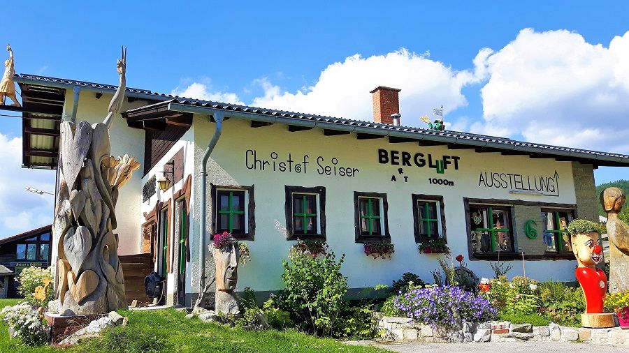 Ein Gebäude mit der Aufschrift 'Bergluft' und Holzskulpturen im Vordergrund.