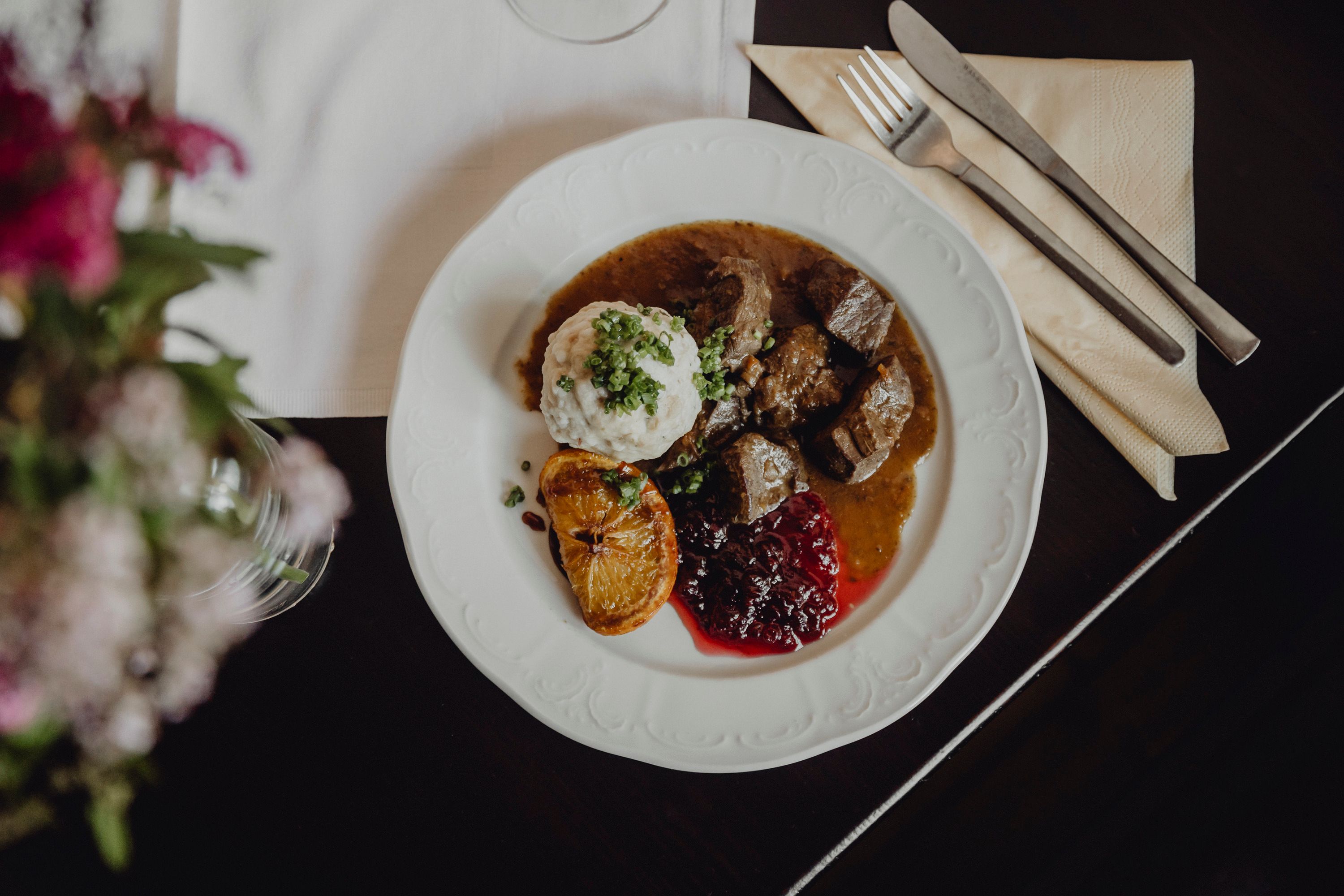 Ein Teller mit Hirschragout, Knödel, Preiselbeeren und einer gebratenen Zitronenscheibe.