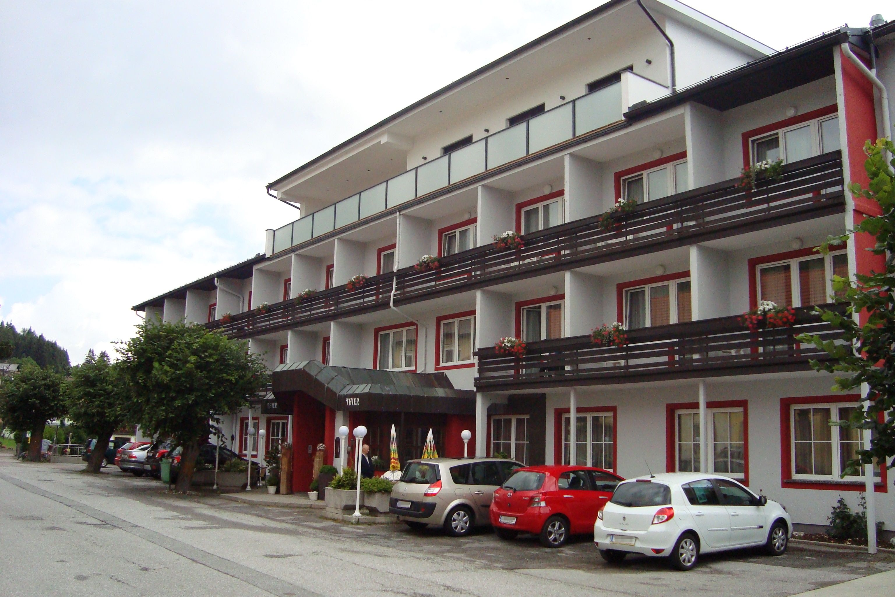 Außenansicht des Hotel Thier mit geparkten Autos und Balkonen mit Blumen.