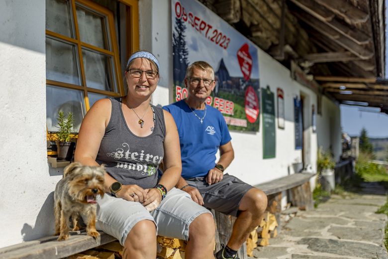 Zwei Personen sitzen vor einem Gebäude mit einem Hund, im Hintergrund ein Plakat mit Datum 09. Sept. 2023.
