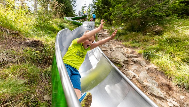 Kind rutscht auf einer Metallrutsche im Freien.