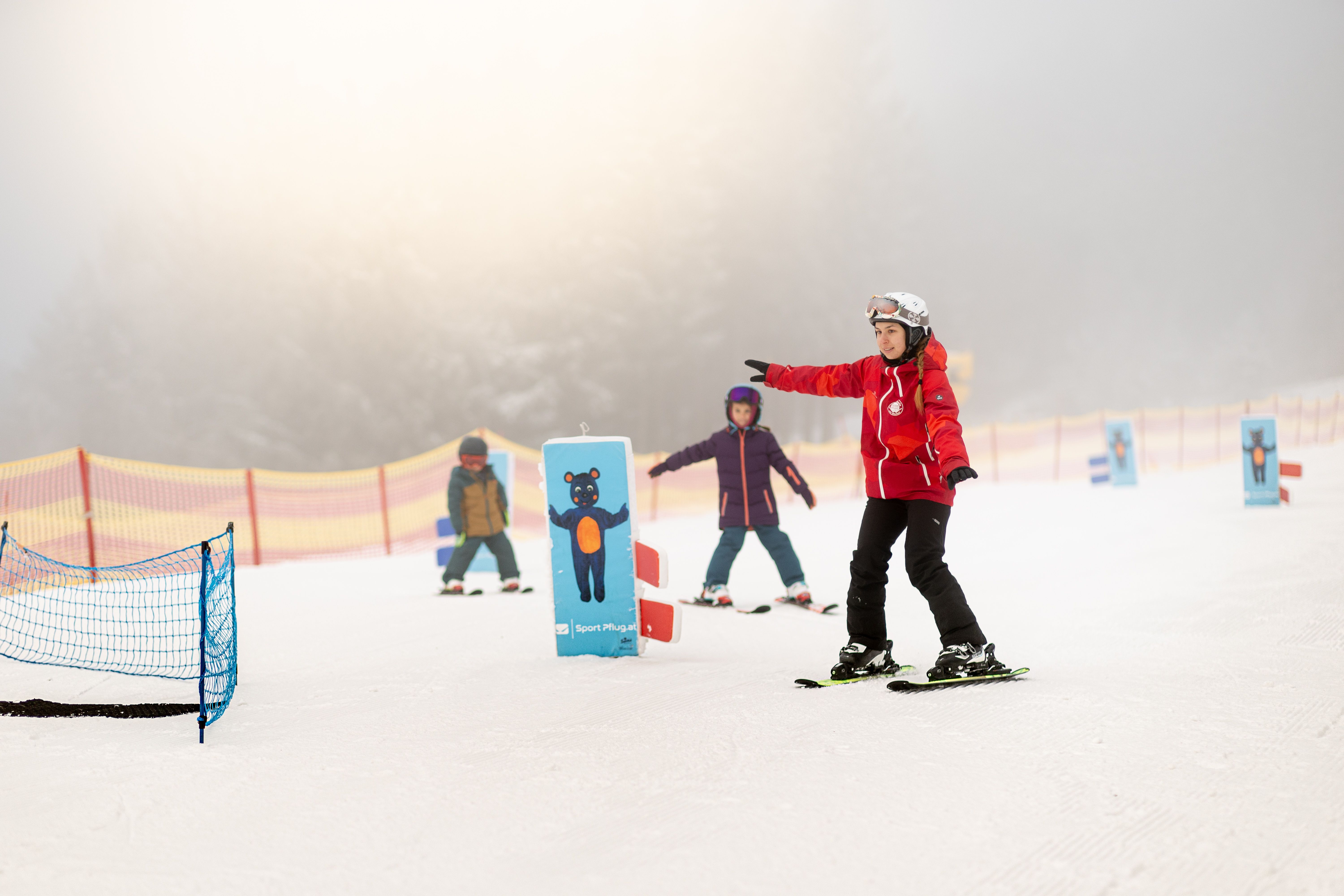 Skilehrerin zeigt einem Mädchen im Kinderland eine Skiübung vor.