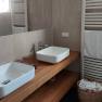Modern bathroom with two white washbasins on a wooden top, towel rail and basket with towels.