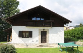 Ein wei&szlig;es Haus mit Holzbalkon und Tischtennisplatte im Garten.