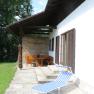Terrace with lounger and wooden furniture next to a house with a shingle roof.