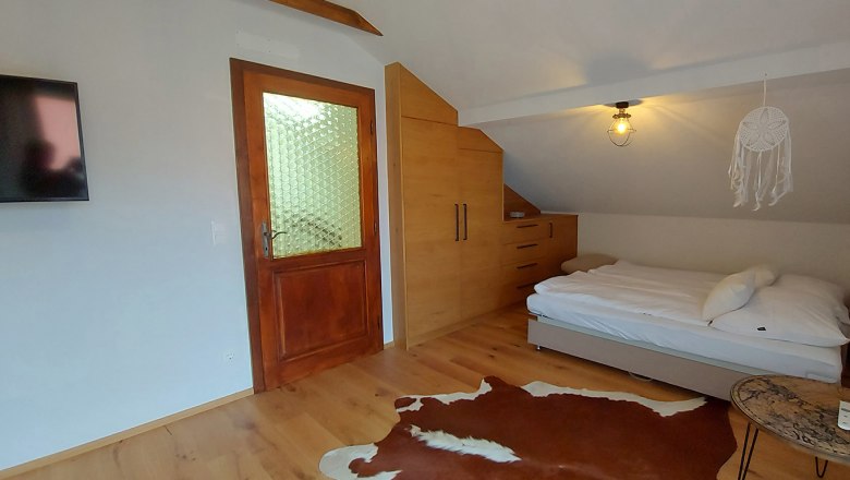Bedroom with wooden floor, bed, wardrobe, door and TV.