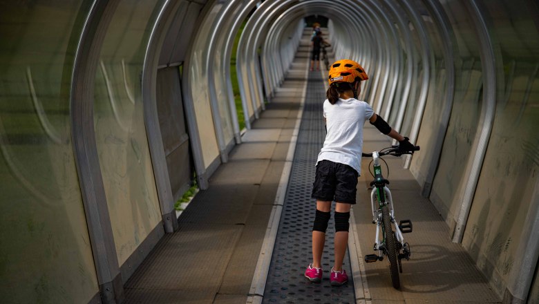 Kind mit Fahrrad auf F&ouml;rderband im &uuml;berdachten Tunnel.