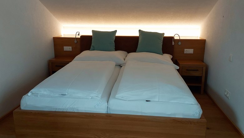 A double bed in a room with a sloping ceiling, two pillows and bedside tables.