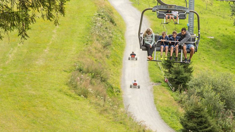 Familie fährt mit dem Sessellift und sieht den Mountaincarts unter ihnen zu