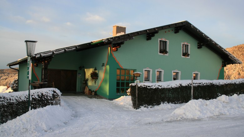 Grünes Haus im Schnee mit dekorativen Elementen und Laterne.