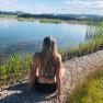 Person sitting on the bank of a pond with a view of the water and the surrounding landscape.